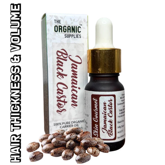 A glass bottle of "Jamaican Black Castor Oil" sits on a white surface, next to a small, square cardboard box containing "Jamaican Black Castor Seeds." from the brand the organic supplies. 